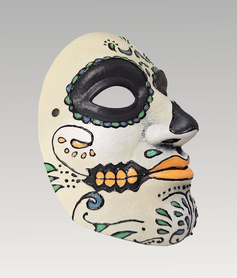 A colorful and intricate Day of the Dead (Día de los Muertos) mask with a white face, black and orange accents, and various decorative elements.