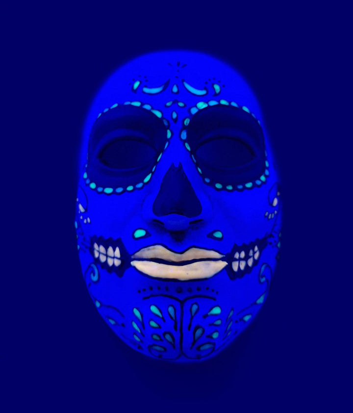 A colorful, intricate face painted in blue and green against a dark blue background.