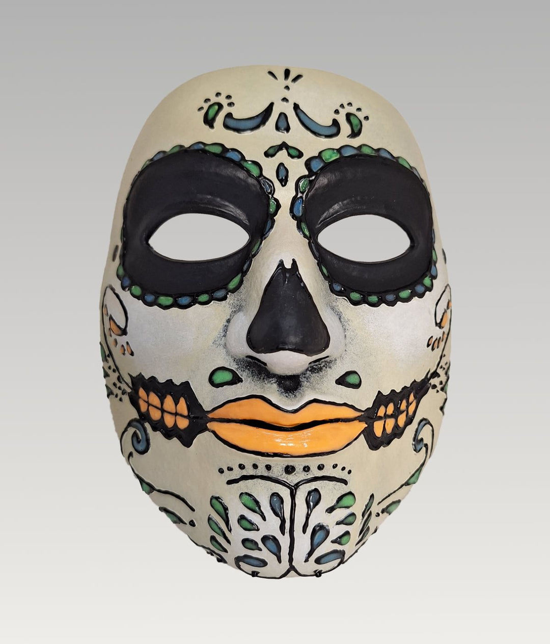 A colorful and intricate Day of the Dead (Día de los Muertos) mask with a white face, black and orange accents, and various decorative elements.